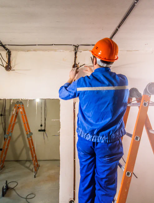 electrician in hard hat and uniform standing on step ladder